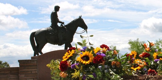 Jennifer Rogers Etcheverry stands beside the Will Rogers Memorial statue, with a commemoration wreath