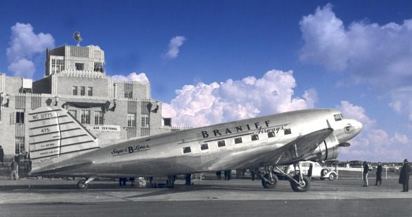 A black and white photo of a Braniff airplane parked on the tarmac in Oklahoma City with a blue sky with clouds background.