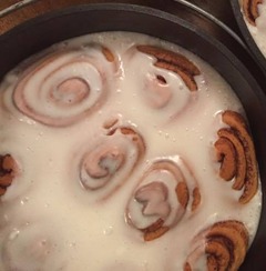 3 dutch ovens, each with cooked and iced cinnamon rolls inside. In the photograph, we are looking down on the cast iron vessels.