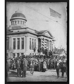 The Carnegie Library on statehood day 1907. The front columns are decorated, the American flag is flying, and people are gathered around the building.
