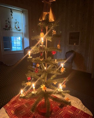 A Christmas tree with simple 1800s-era decorations sits on a table with candles lit