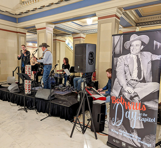 A photo of Kyle Dillingham and his group performing at the Oklahoma State Capitol with a Bob Wills Day banner in the foreground