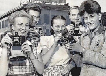 A group of teenagers holding cameras and smiling. The photo is Black and White.