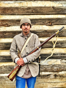 Seth Goff poses with a musket from the Civil War era with a log cabin in the background.