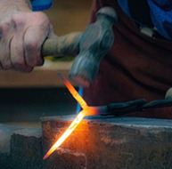 A close up view of Tom Nelson hammering a red hot piece of iron on an anvil