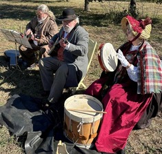 A group of musicians playing Civil War-Era musical instruments in period clothing. They are seated outdoors.
