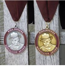 A series of Will Rogers medallions hanging on a fence. The face of Will Rogers can be seen on the gold, bronze and silver medallions.