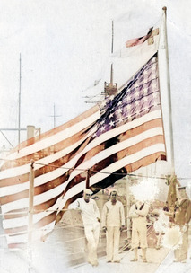 A flag flying on deck of the USS Oklahoma with members of the crew in the foreground. The flag has been colorized.