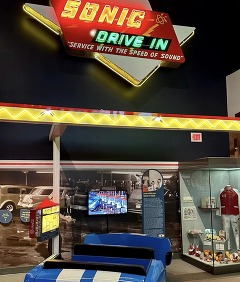 Sonic Drive in exhibit at OHC, including seating within a blue Mustang parked in front of an exhibit of a Sonic Drive-In lighted menu sign