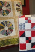 Two quilts draped over displays. One is a pinwheel design, and the other is made in patriotic colors.