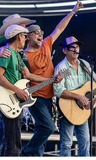 Red Dirt Rangers performers all singing into the same microphone with hands raised and guitars in hand.