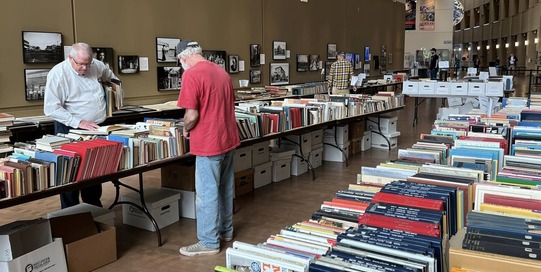 Photo of people looking at tables full of books at the Oklahoma History Center. The Space exhibit can be seen in the background