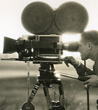 A man films behind a large reel to reel camera