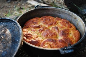 Cinnamon Rolls in a cast iron dutch oven. They are golden brown, cooling off of the fire.