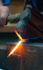 A Blacksmithing demonstration. The photo details a red hot iron bar being pounded into shape on an anvil