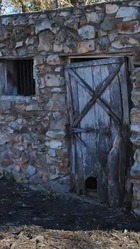 A jailhouse in Disney, Mayes County. A rock and mortar structure with bars covering a small window and a wooden door