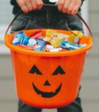 A young boy wearing a skeleton costume, holding a trick-or-treat pail full of candy