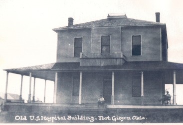 An historic photo of the Fort Gibson hospital. Two men are seated on the wrap around porch