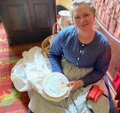 A Hunters Home historian sitting in period dress with an embroidery project in her hands