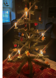 A tabletop Christmas tree with small paper, natural decorations, and clipped candlelights. The candles are lit