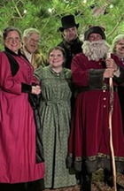 A group of people gathered at a large decorated Christmas tree in Victorian clothing