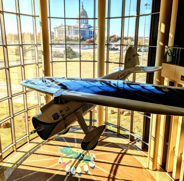 The Oklahoma History Center Devon Great Hall with a photo of the Oklahoma Capitol at a distance and the Winnie Mae airplane at center