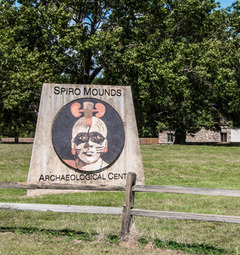 The entrance to the Spiro Mounds Archaeology Center in Spiro. A sign depicting an artist's version of  person in the Mississippian period