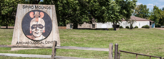 The entrance to the Spiro Mounds Archaeology Center in Spiro. A sign depicting an artist's version of  person in the Mississippian period