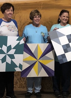 Women holding wooden squares that have been painted into barn quilts