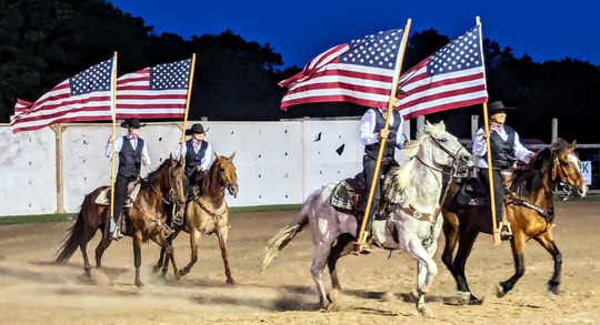 Riders in a performance at the Pawnee Bill Wild West Show, riding horseback in uniforms with American flags streaming