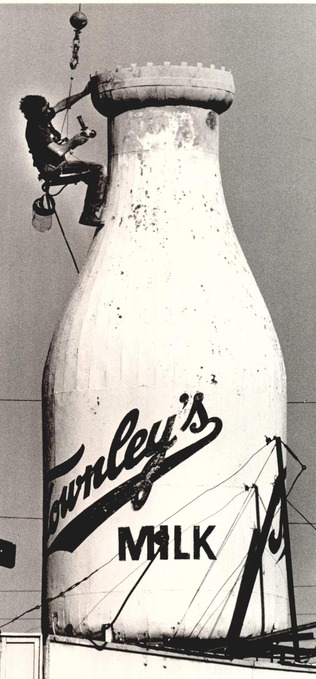 A worker gets ready to paint the triangle grocery building oversized milk bottle feature