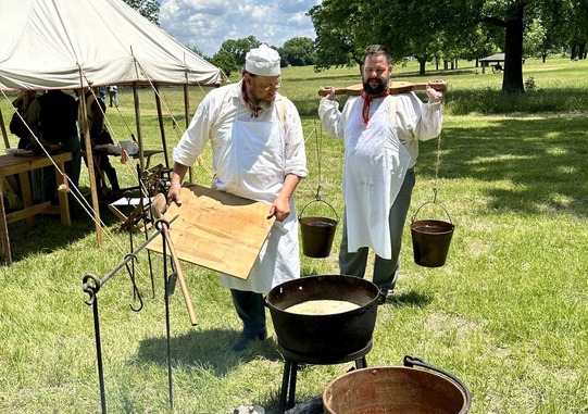 Dave Fowler and Chantry Banks bring water to the campsite where two dutch ovens are heating over a fire