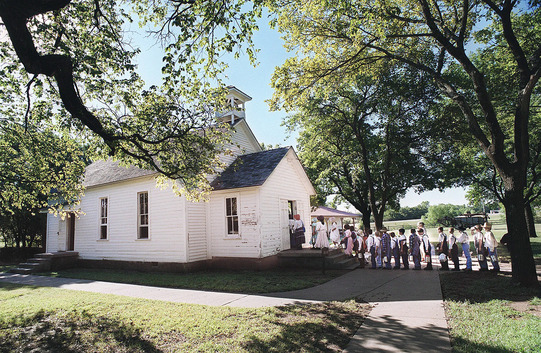 A photograph of Schoolchildren entering Rose Hill School. A line of students is formed outside the schoolhouse