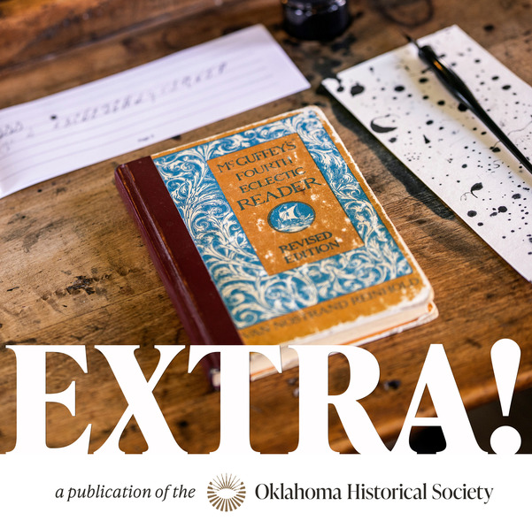 A McGuffey's Reader, a penmanship practice booklet, a blotting paper with ink spots and a quill pen on the surface of a wooden desk