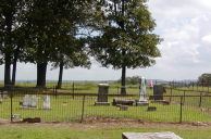 A country cemetery fenced in on all sides with a variety of monuments placed over time