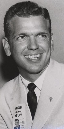 A young George Nigh dressed in a suit and tie, with a campaign ribbon that says "Nigh is the Guy" pinned to his suit's lapel