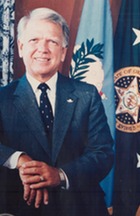 Oklahoma Governor George Nigh standing in front of the flag of Oklahoma
