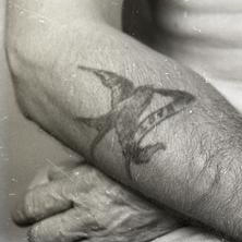The detail of a swallow tattoo on a man's arm. The image is black and white