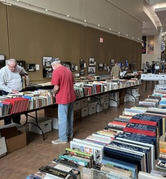 Two men peruse the selection of books laid out on tables at the Oklahoma History Center. The scene depicts the annual book sale.