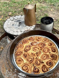 Cinnamon Rolls cooked in a dutch oven with a pot of coffee over an open fire