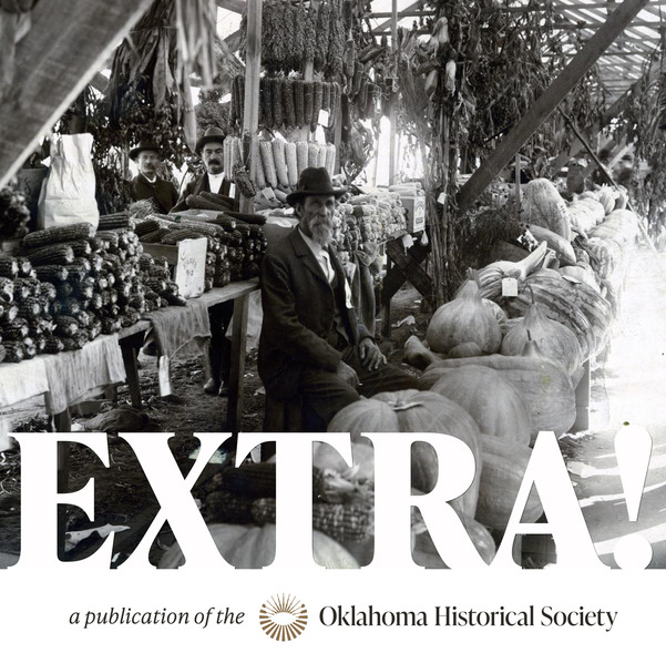 A farmer stands behind his vegetable market with large pumpkins, squash and corn on display, October 1898. Other people can be seen in the background
