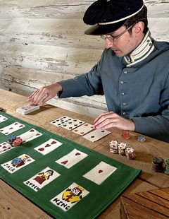 A living history actor plays with a card deck replica like those used in the Civil War era. Dice and chips are also on the table.