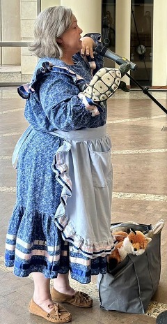 An Indigenous storyteller stands in front of a microphone in the great hall of the Oklahoma History Center