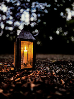 A candle lit inside a glass lantern sits on the trail in Doaksville with leaves around it