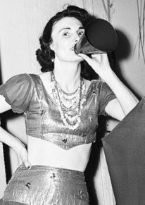 A photograph of a woman in a costume with a megaphone and painted billboards with balloons and streamers behind her