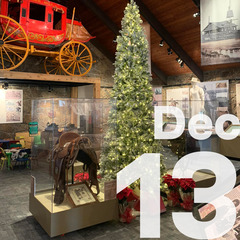 An exhibit area with a stagecoach and saddles, with a Christmas tree at its center.