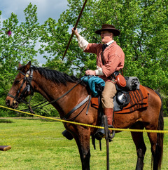 A man dressed in Civil-War era clothing holds a weapon aloft on horseback.
