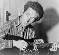 Woody Guthrie plays a guitar with a sticker that reads "This Machine Kills Facists" 