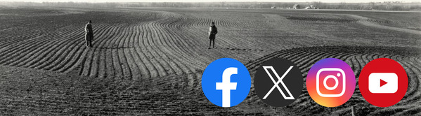 Two figures stand in the middle of a field with deep furrows of soil stretching as far as the eye can see. A barn and home are in the distance