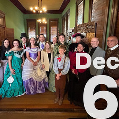 A group gathered in Victorian costumes, forms a horseshoe grouping.